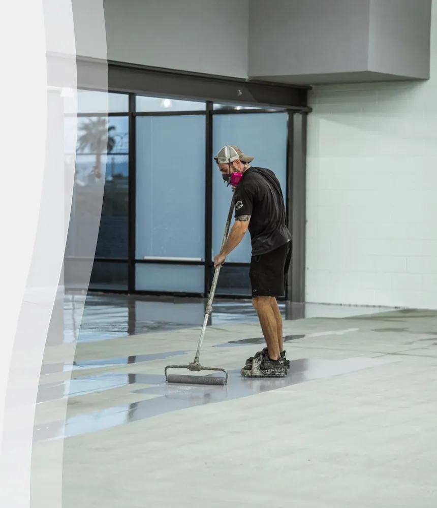 Epoxy flooring technician applying a smooth base coat to a commercial concrete surface